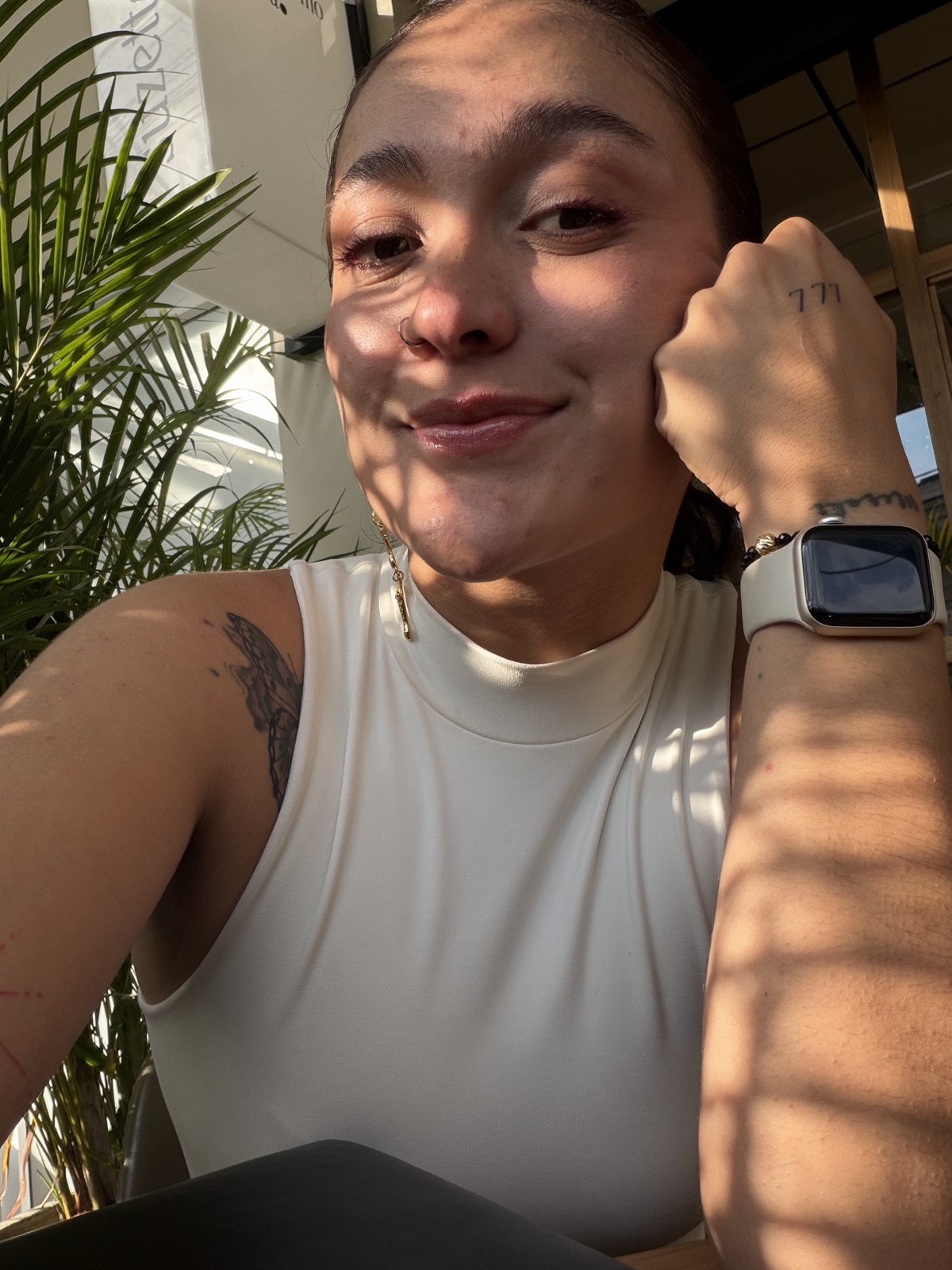 Nadia sonriendo en un café, con la mano en el mentón, en luz cálida moteada.